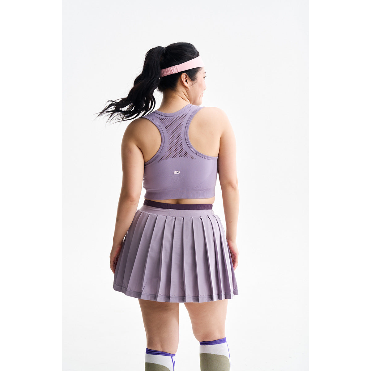 Rear view of a model wearing a lavender racerback sports top and matching pleated skirt.
