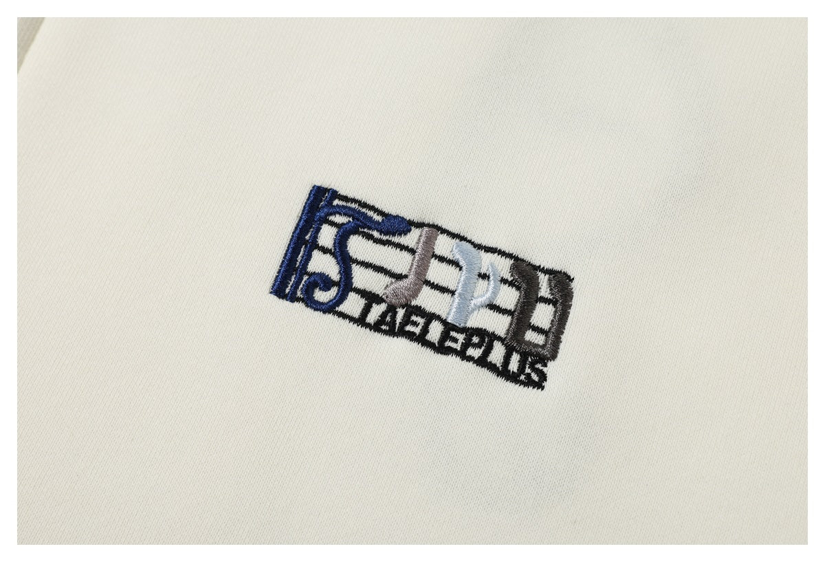 Close-up of a small multicolor embroidered musical motif on ivory jacket fabric.