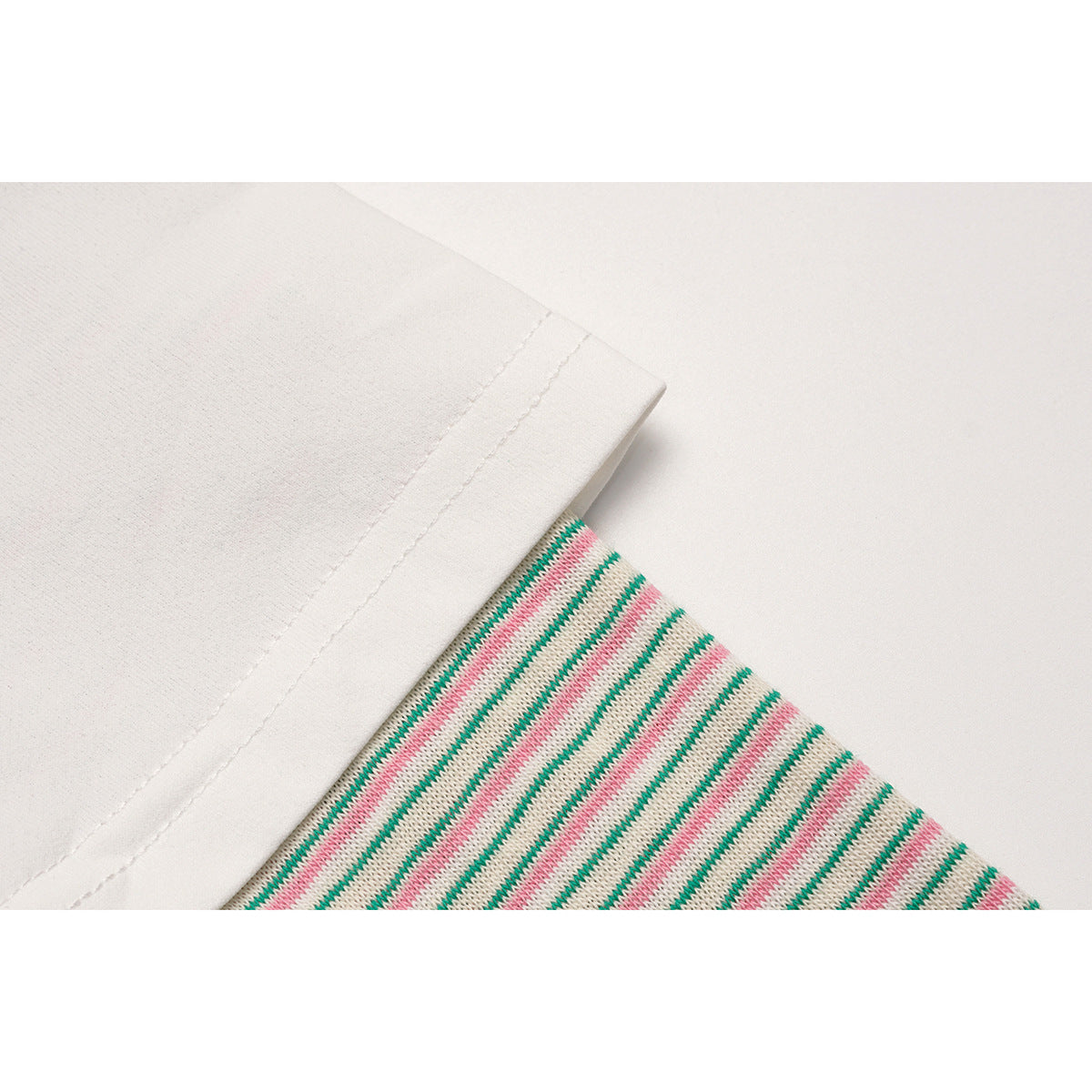 Close-up of a white hem beside a long sleeve with thin green and pink stripes.