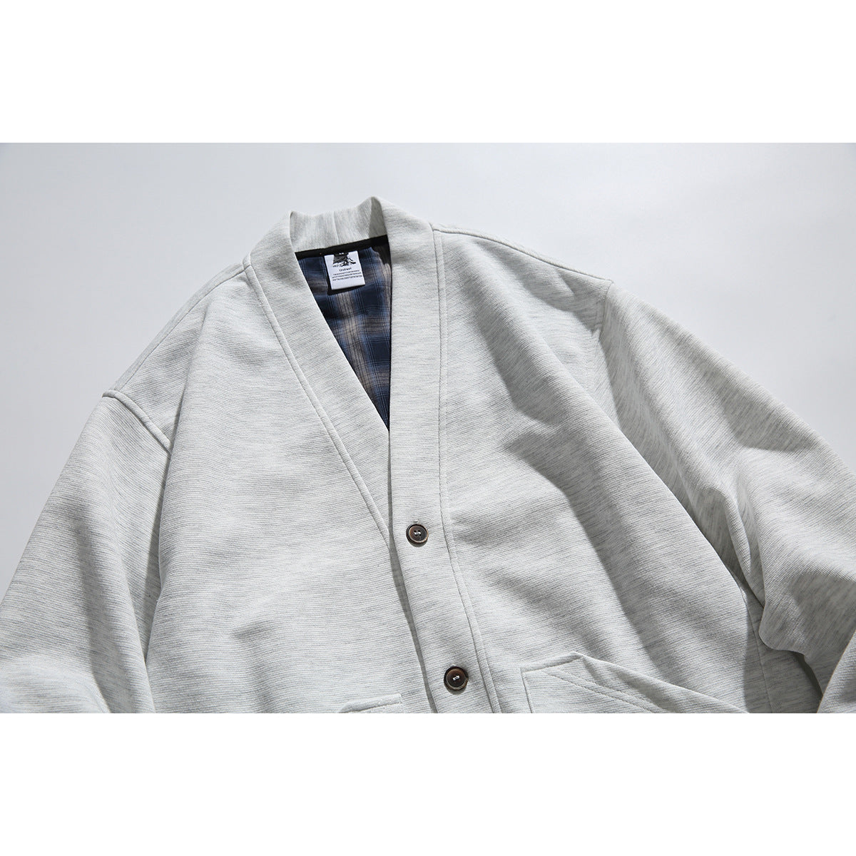 Close front view of a light gray button-front cardigan with a shawl collar, plaid inner facing, and patch pockets.