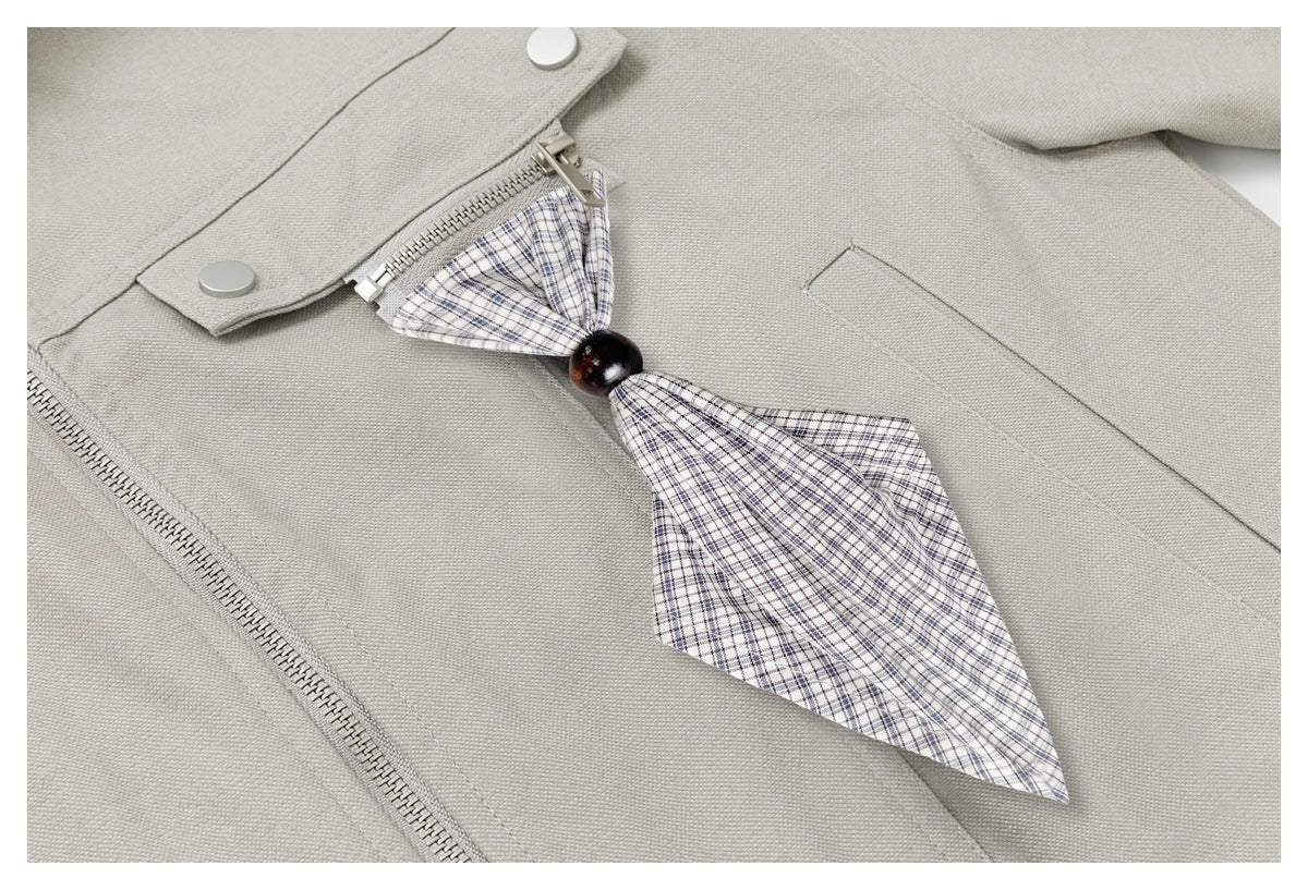 Close-up of a light beige jacket with a plaid neck detail held by a dark bead.