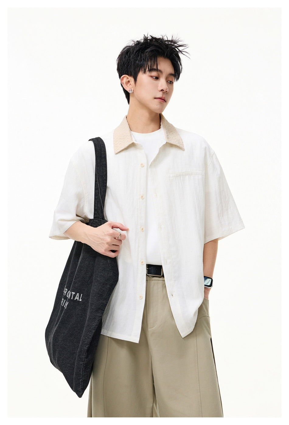 Model wearing an ivory short-sleeve shirt with a beige textured collar and chest pocket, carrying a dark tote.