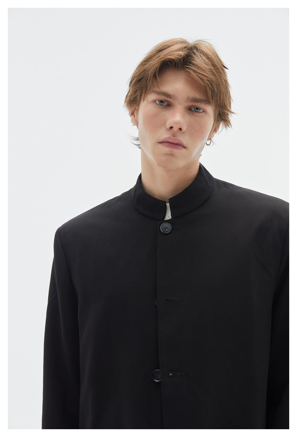 Close-up of a model wearing a black stand-collar jacket with a large dark button and concealed front fastening.