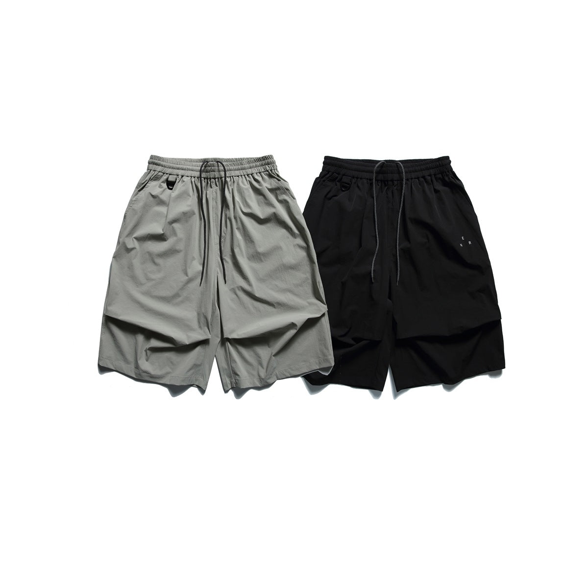 Loose, knee-length shorts shown in gray-green and black, with elastic drawstring waistbands and small D-rings.