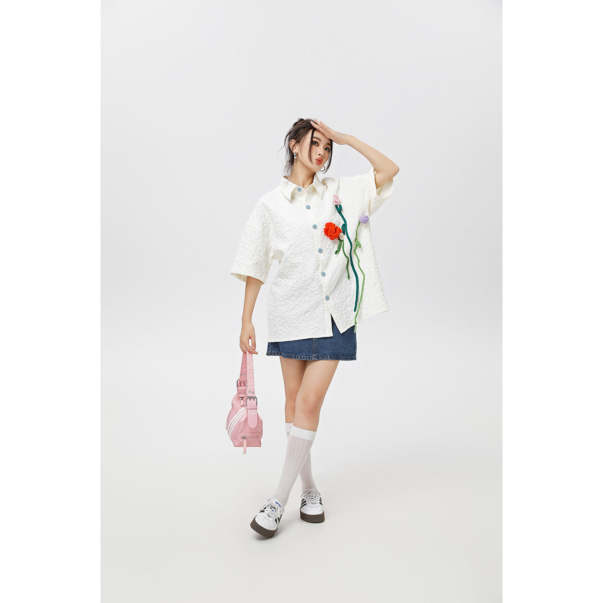 Model wearing an oversized white short-sleeve button-up shirt with colorful flower appliqués, denim skirt and knee socks.