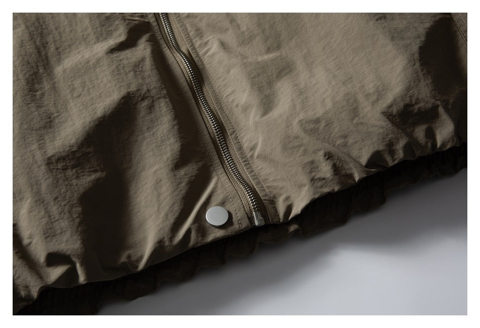 Close-up of an olive-brown jacket's front zipper and metal snap near the hem.