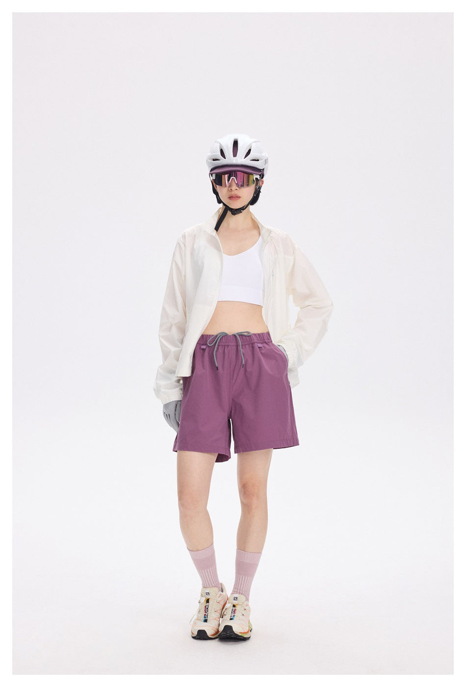 Model wearing an open white stand-collar jacket with a white top, purple shorts, helmet and sneakers