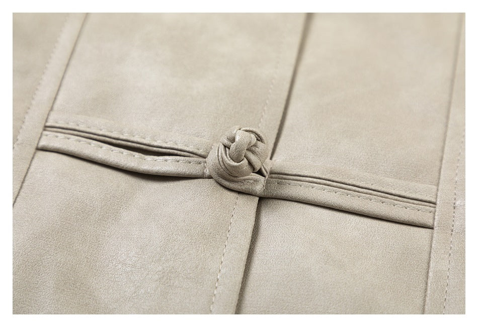 Close-up of a knotted fabric closure and stitched panels on a light taupe coat.