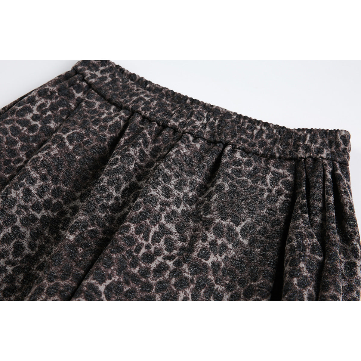 Close-up of dark brown and black leopard-print trousers with a gathered elastic waistband and front pleats.