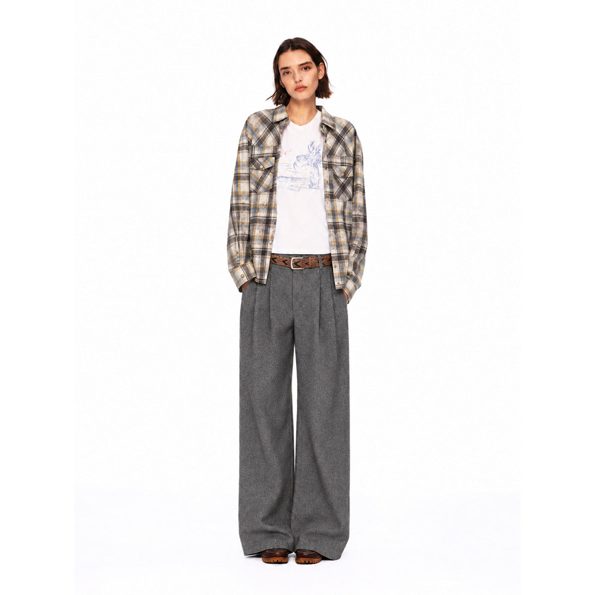 Model wearing an open beige, gray and blue plaid shirt over a graphic white tee with gray wide-leg trousers.