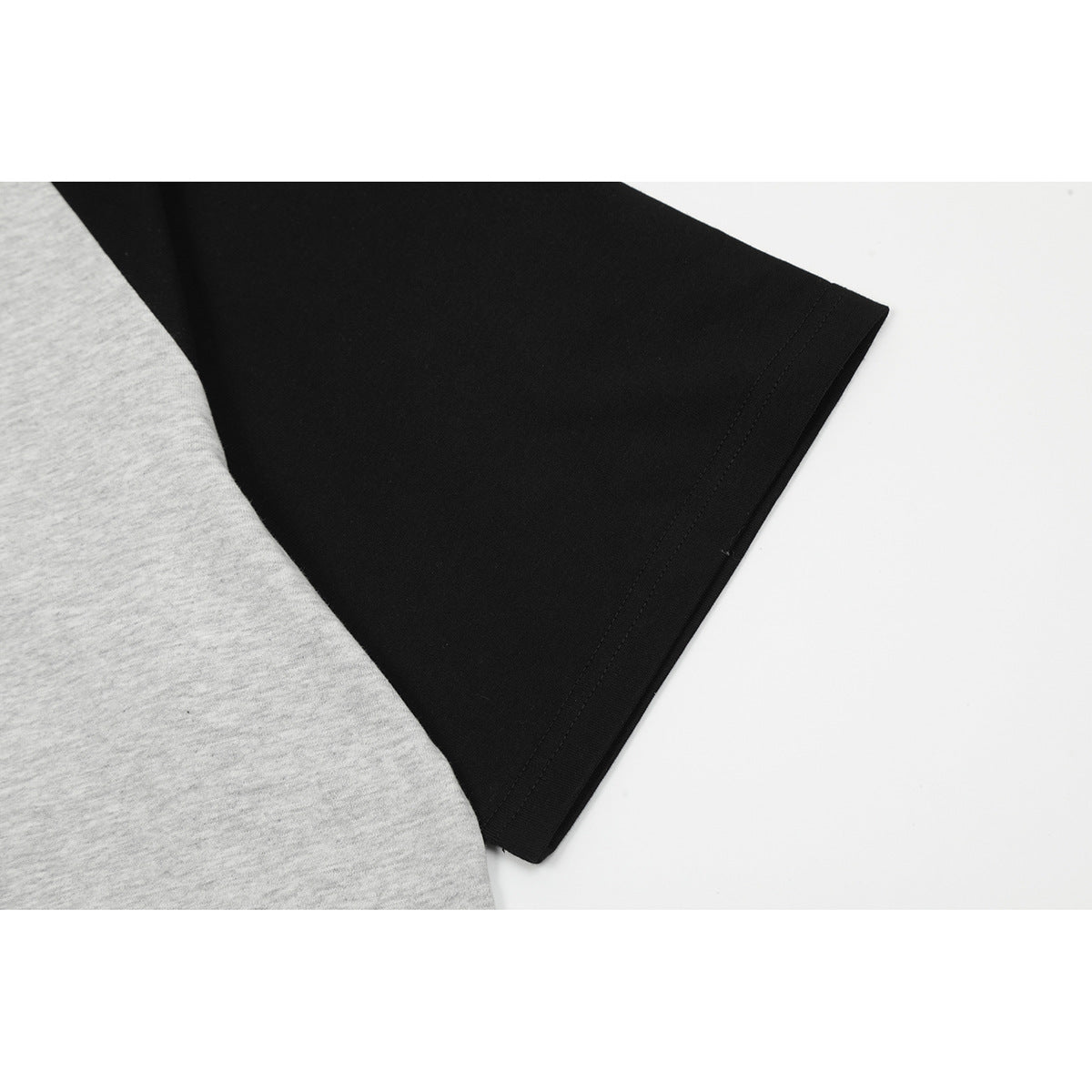 Close-up of the black short sleeve and stitched hem beside the heather gray body of a raglan T-shirt.