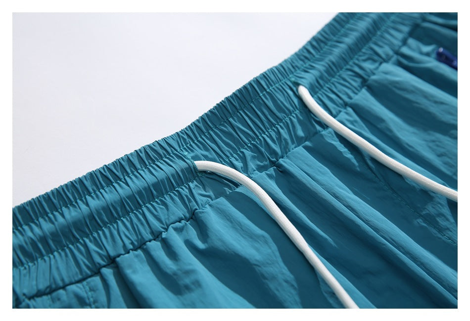 Close-up of teal shorts with a gathered elastic waistband and white drawcords.