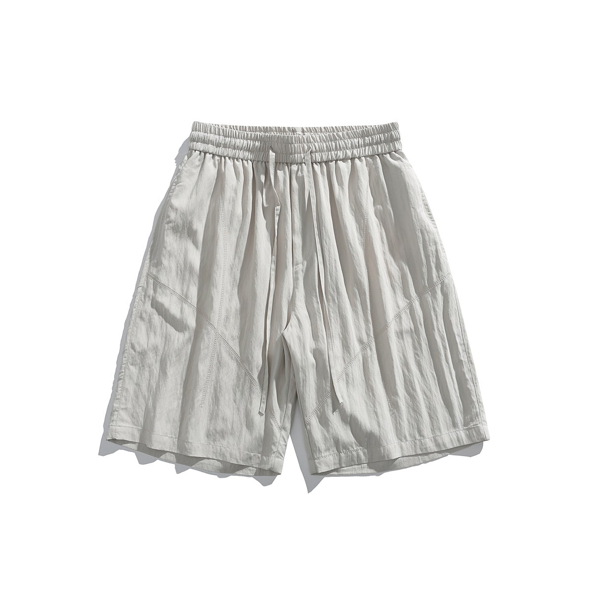 Front view of off-white loose shorts with a gathered elastic waistband, drawstring, and angled seam panels.