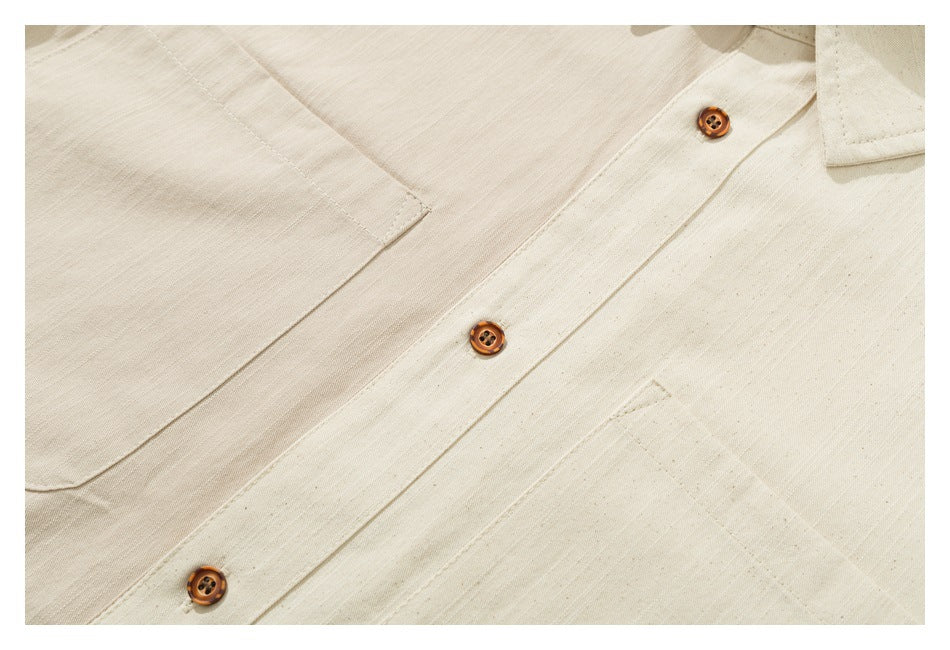 Close-up of an ivory shirt front with brown buttons, a chest pocket, and a pointed collar edge.