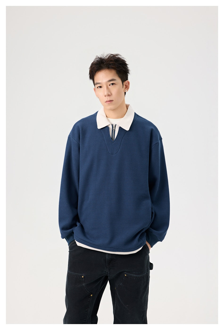 Model wearing a navy pullover with a white collar and short zip placket, shown from the waist up.