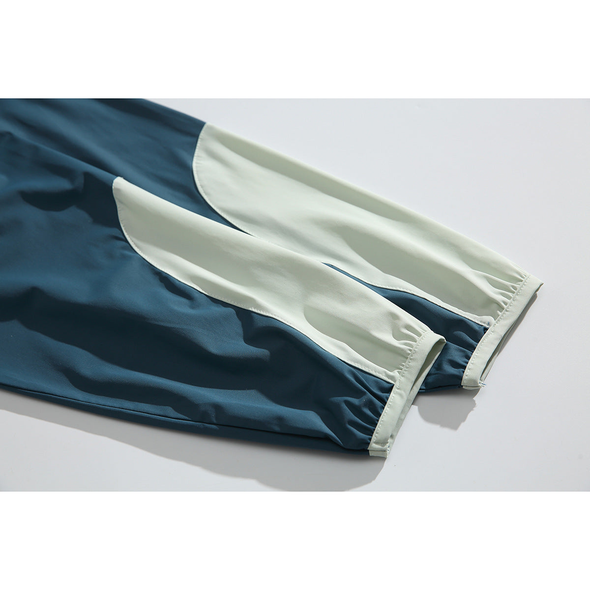 Close-up of two long sleeves with pale contrast panels and matching cuff trim on a teal pullover.