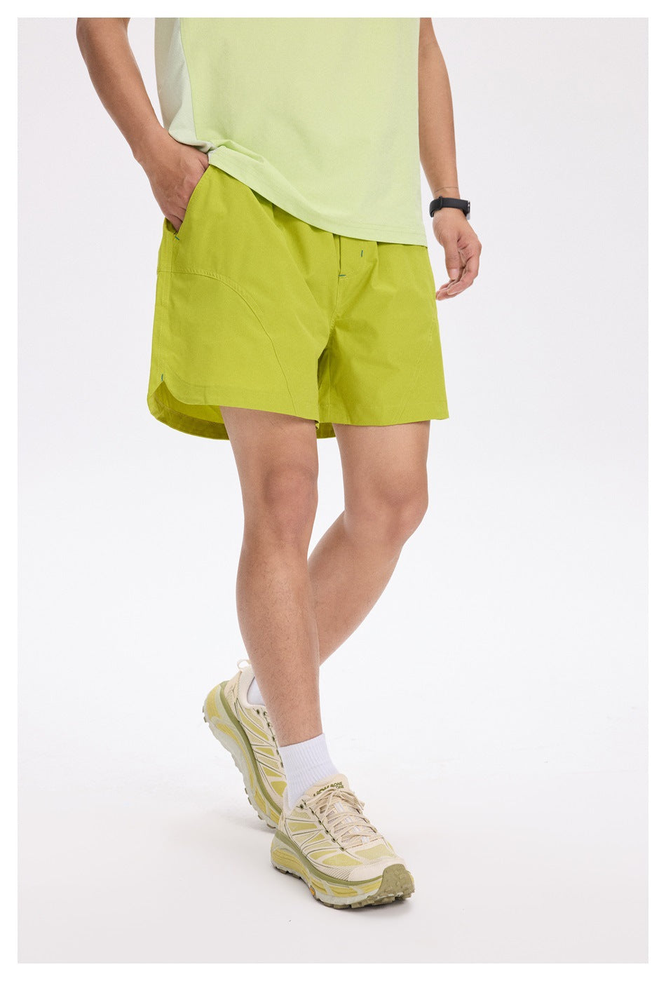 Cropped view of a person wearing lime green running shorts with a pale yellow-green top and sneakers.