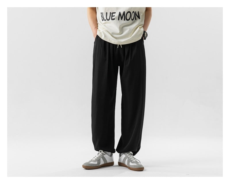 Front view of a model wearing loose black drawstring pants with gathered hems and gray sneakers.