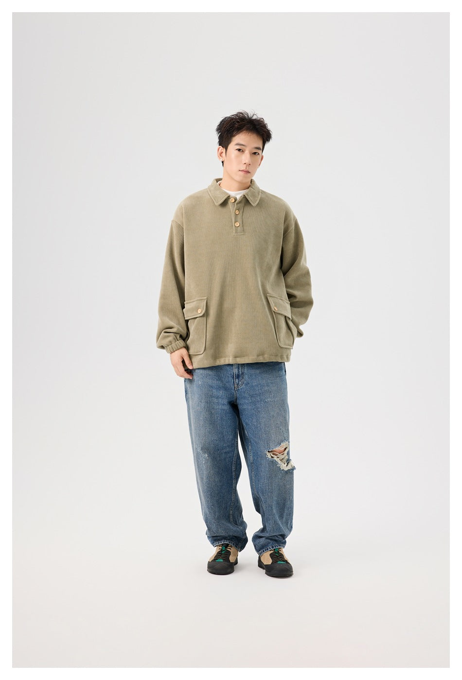 Model standing in the olive polo-collar pullover with button flap pockets, elastic cuffs and distressed blue jeans