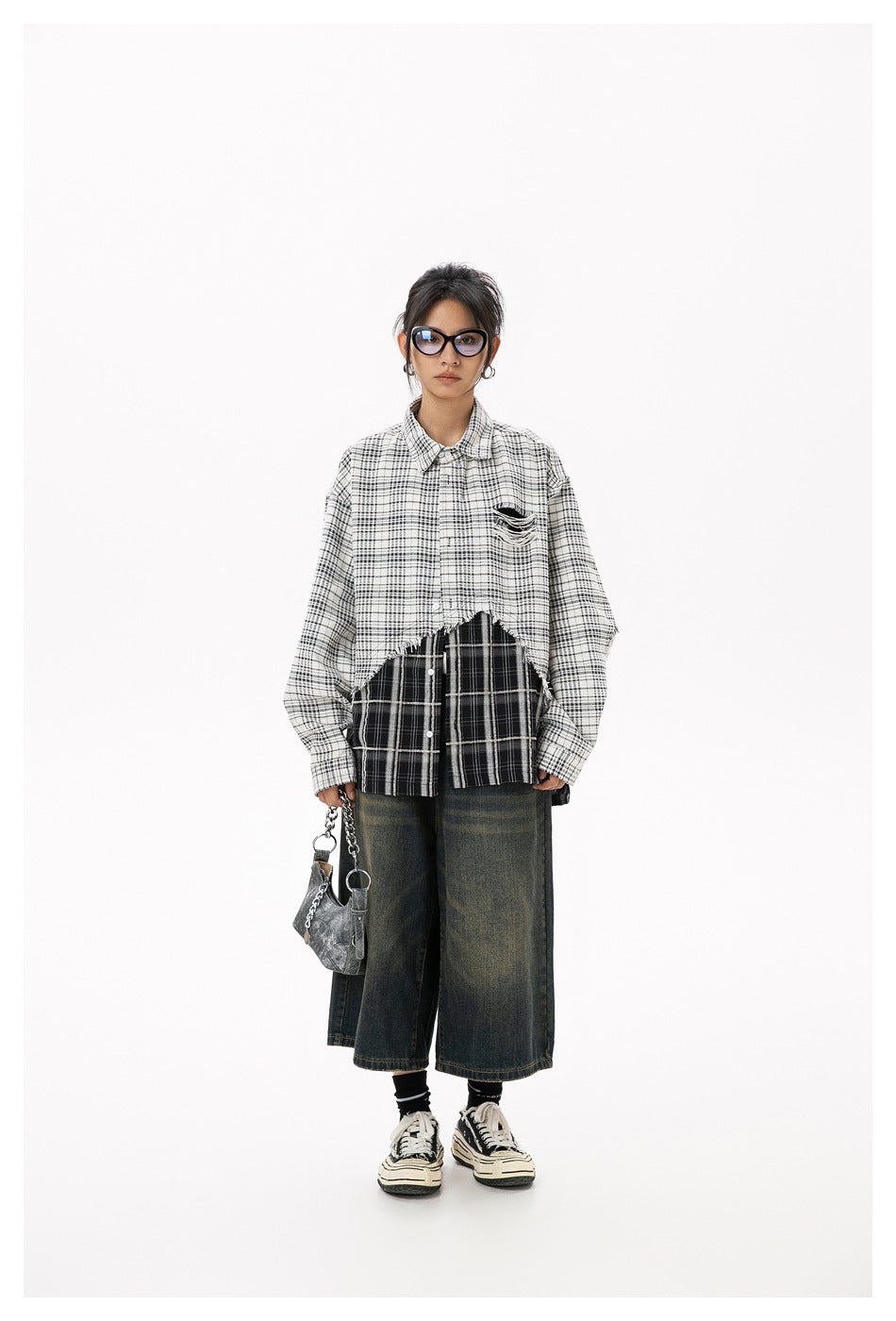 Full-length model wearing an oversized two-tone plaid shirt with frayed hem and dark wide-leg jeans, carrying a small bag.