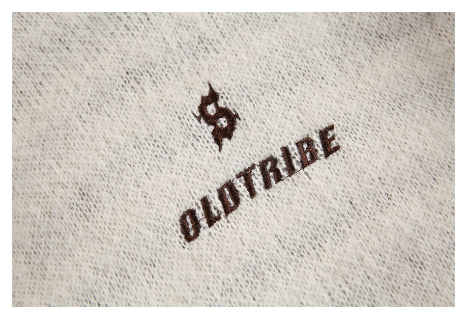 Close-up of dark embroidered lettering and a small emblem on cream knit fabric.