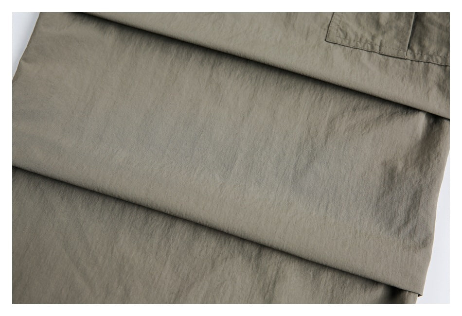 Close-up of olive-gray garment fabric folded in overlapping layers, with part of a pocket visible.