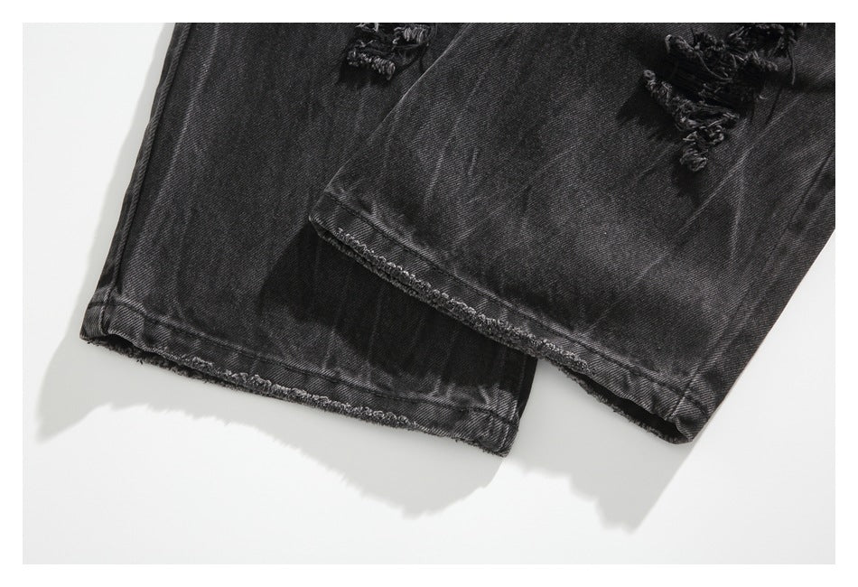 Close-up of charcoal-black jeans showing frayed hems and distressed patches near the cuffs.