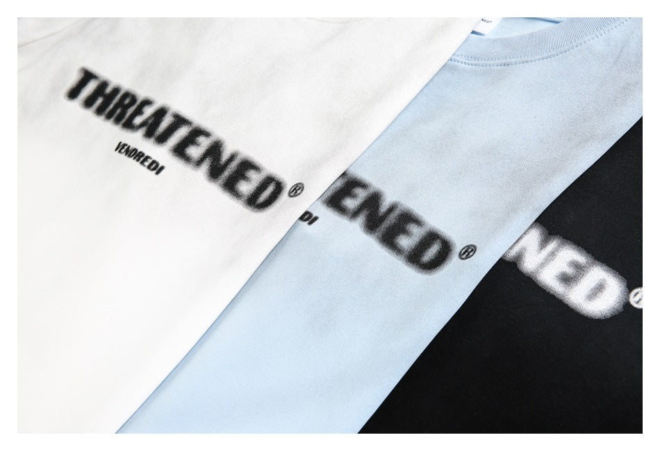Close-up of white, light blue, and black T-shirts with bold printed lettering across the chest.