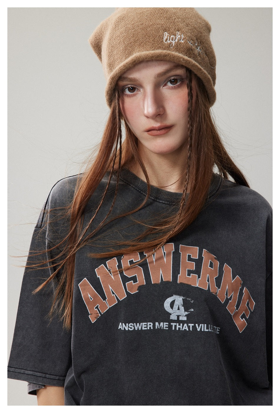 Close-up of a model wearing a charcoal oversized graphic T-shirt and a tan knit beanie.