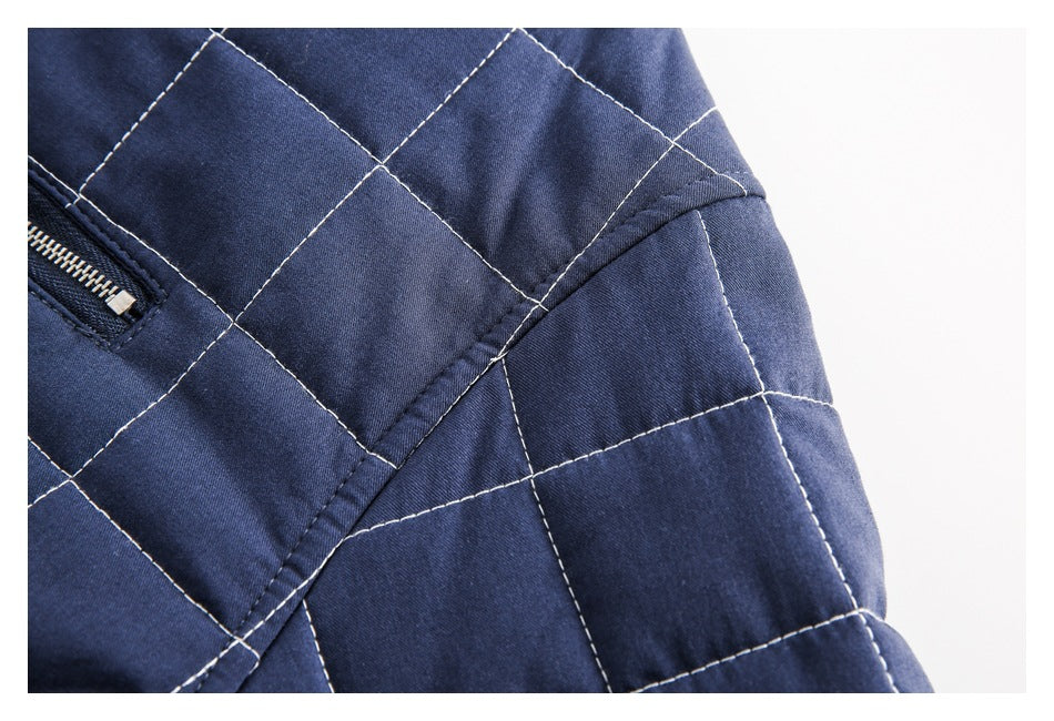 Close-up of navy quilted garment showing contrast stitching and a curved seam beside a zipper pocket.