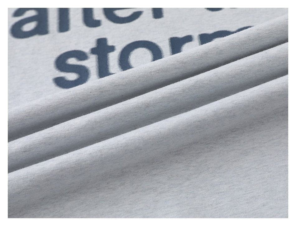 Close-up of light gray printed garment fabric with partial dark lettering and soft folds.