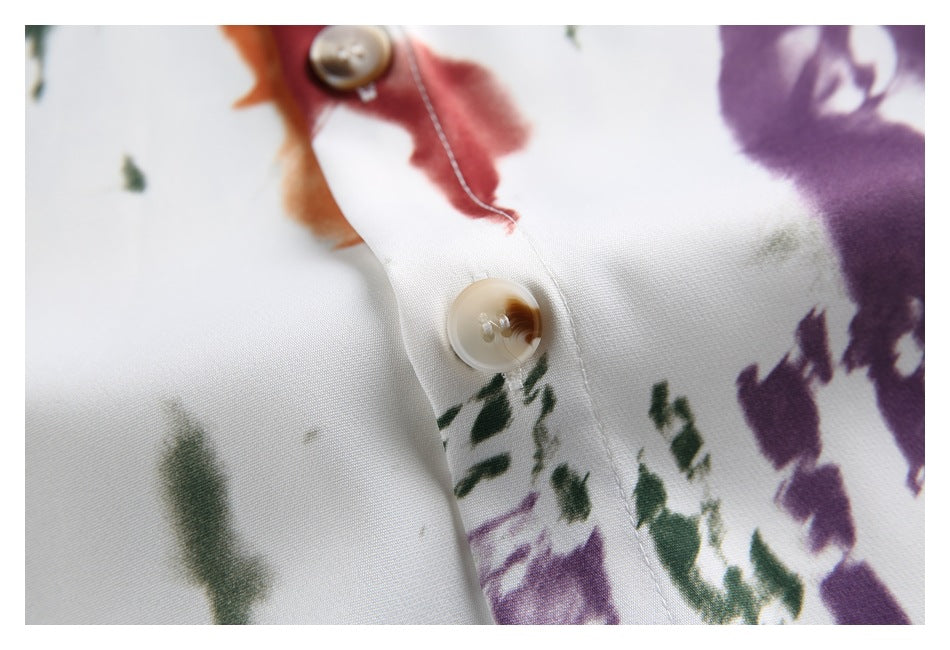 Close-up of a cream shirt's button placket with tan buttons and multicolored abstract brush-print figures.