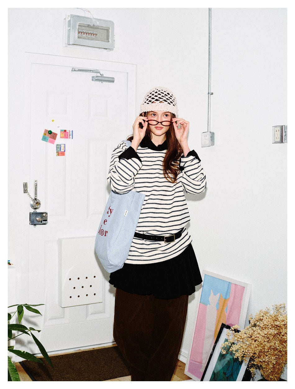 Model wearing a loose cream top with thin black stripes, black collar and cuffs, paired with a black skirt and brown