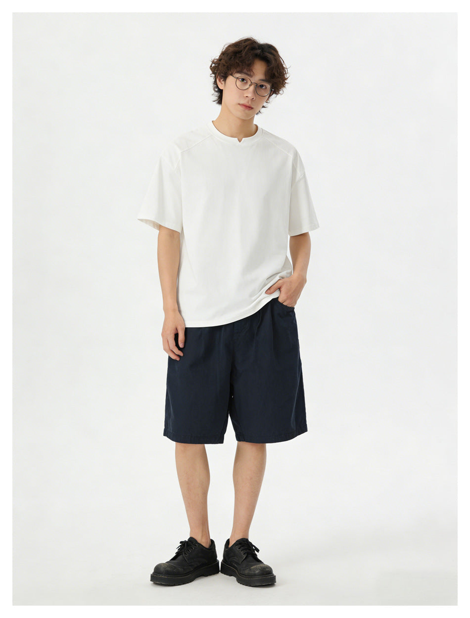 Model wearing a relaxed white V-notch T-shirt with navy shorts and black shoes, hand in pocket