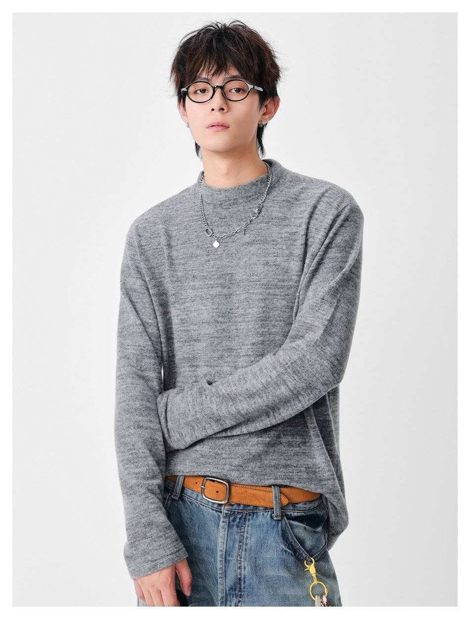Model wearing a heather gray mock-neck long-sleeve top, standing with arms loosely crossed.