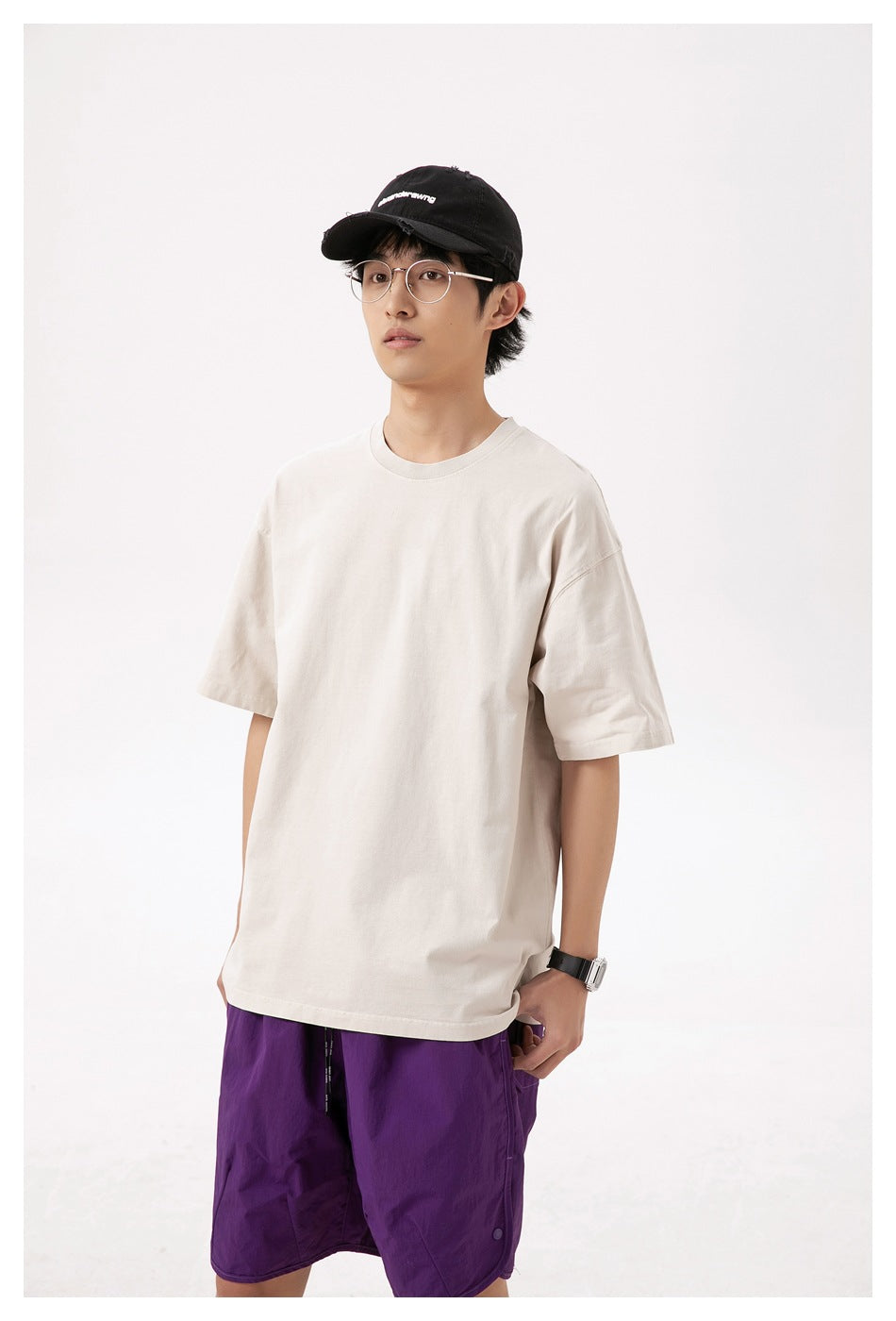 Man in a sand beige short-sleeve crew neck T-shirt with a black cap and purple shorts, three-quarter view