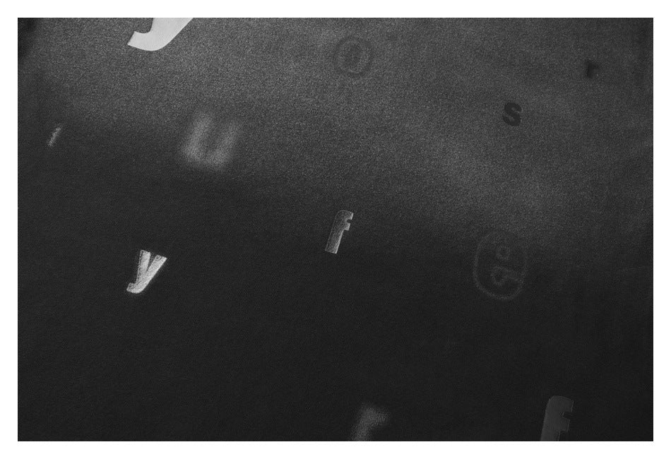 Close-up of black fabric with a scattered, low-contrast pattern of small letters and symbols.