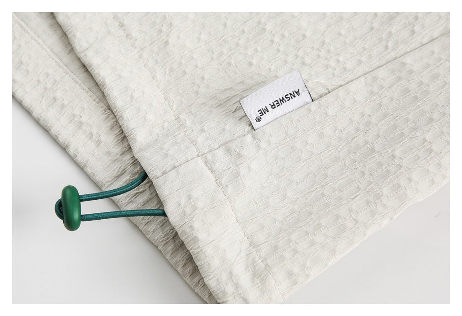 Ivory garment hem detail with a green cord toggle and a sewn English label.