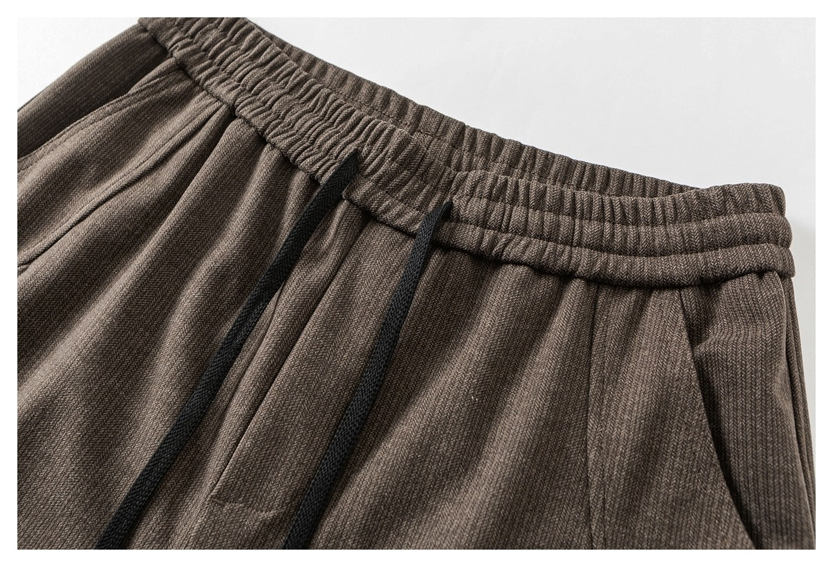 Close-up of taupe trousers showing the gathered elastic waistband and black drawstrings.