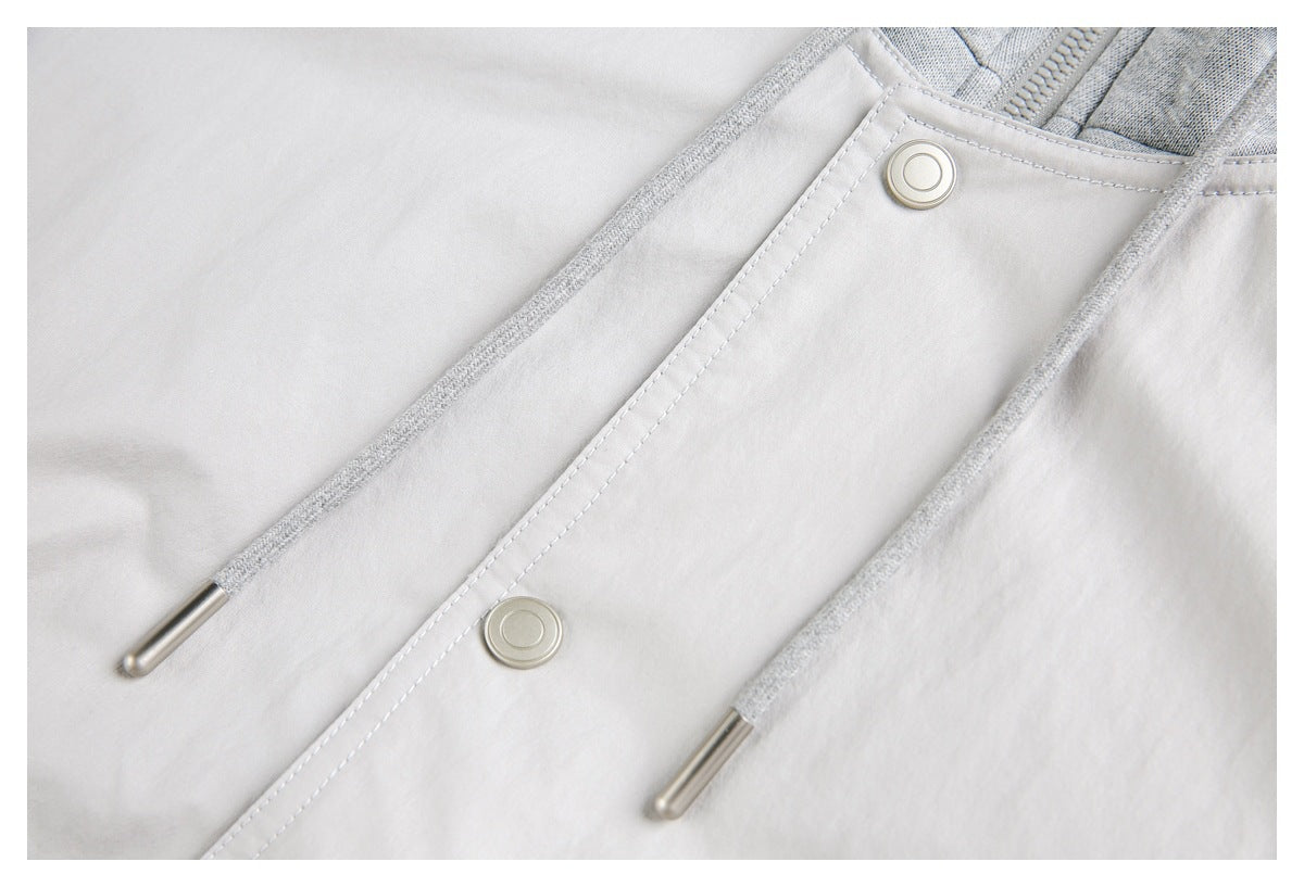 Close-up of a light gray jacket front with drawstrings, metal tips, and two circular snap buttons.