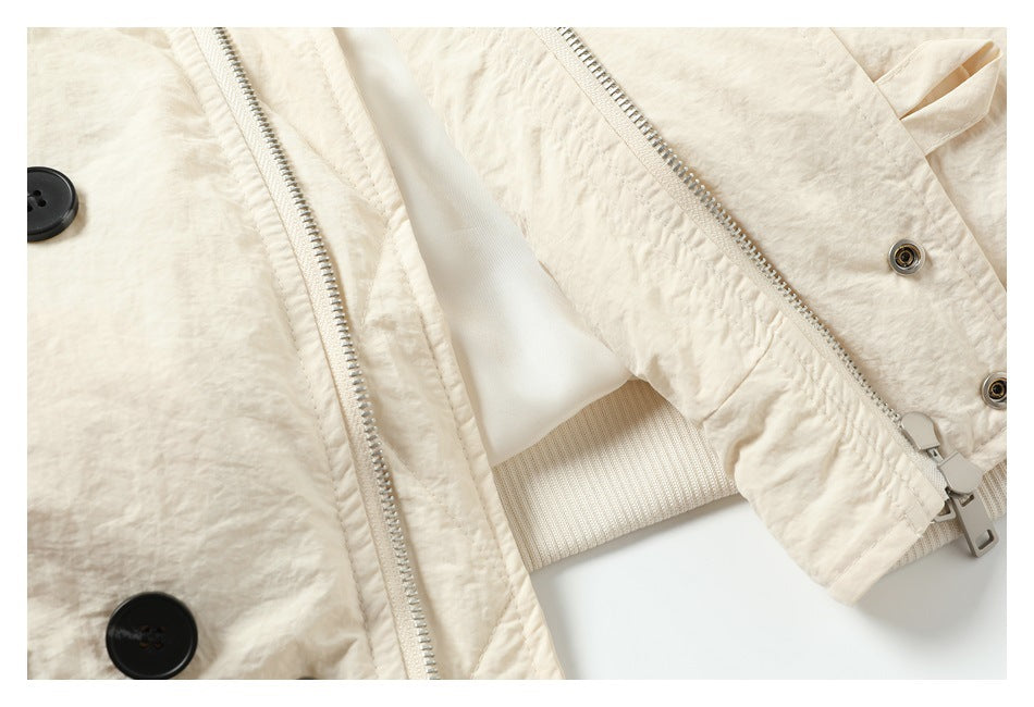 Close-up of cream garment front details: a metal zipper, black buttons, inner lining, and ribbed hem.