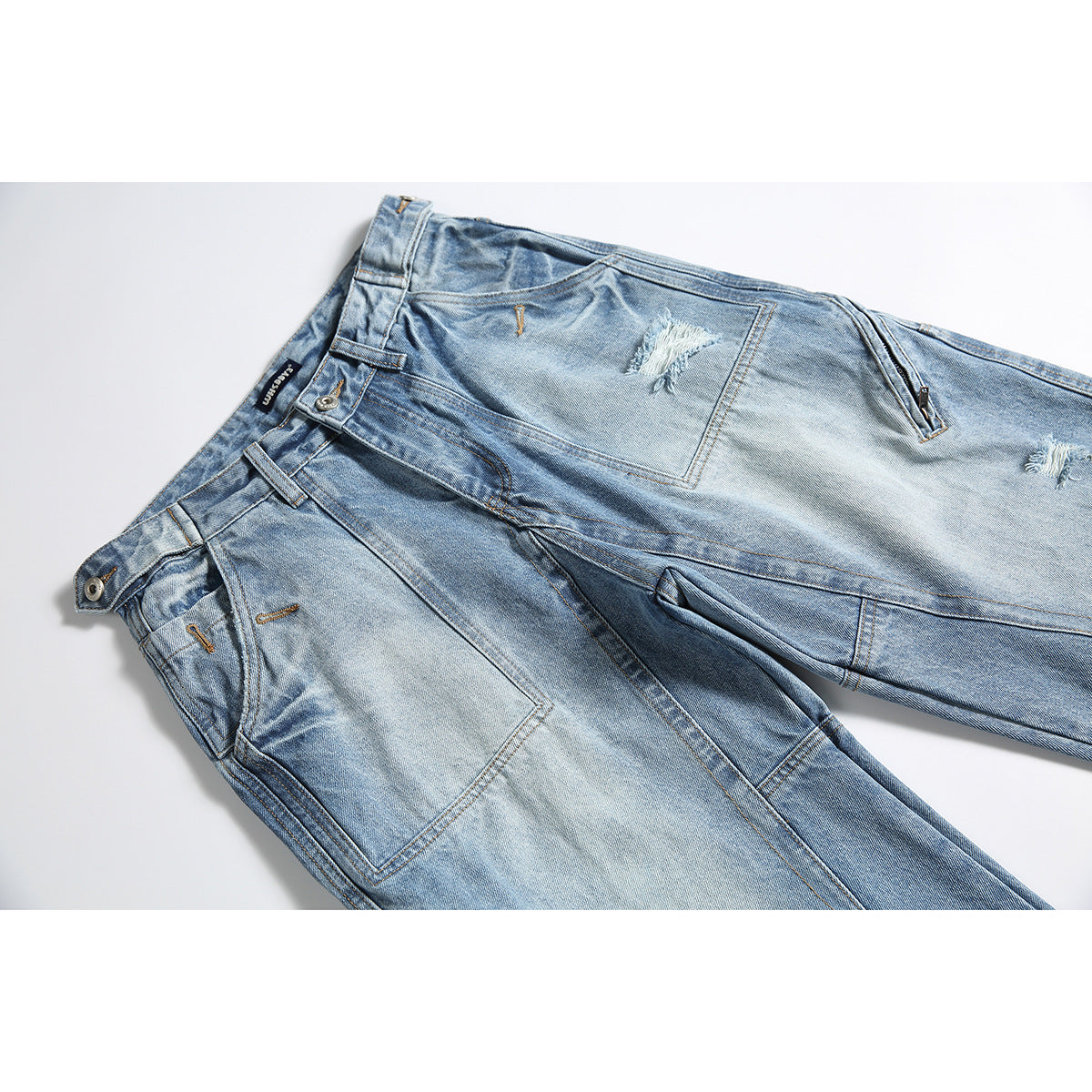 Angled flat lay of light-wash distressed jeans with patch pockets, belt loops, and contrast stitching.