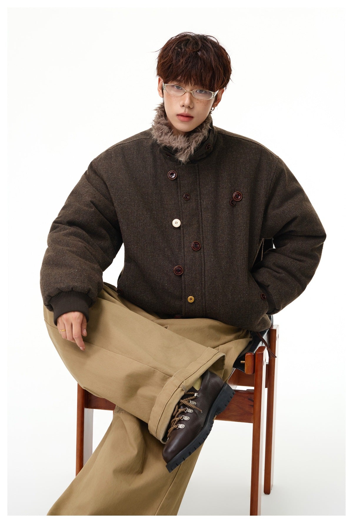 Seated model in a dark brown jacket with a high faux-fur collar, ribbed cuffs and assorted buttons.