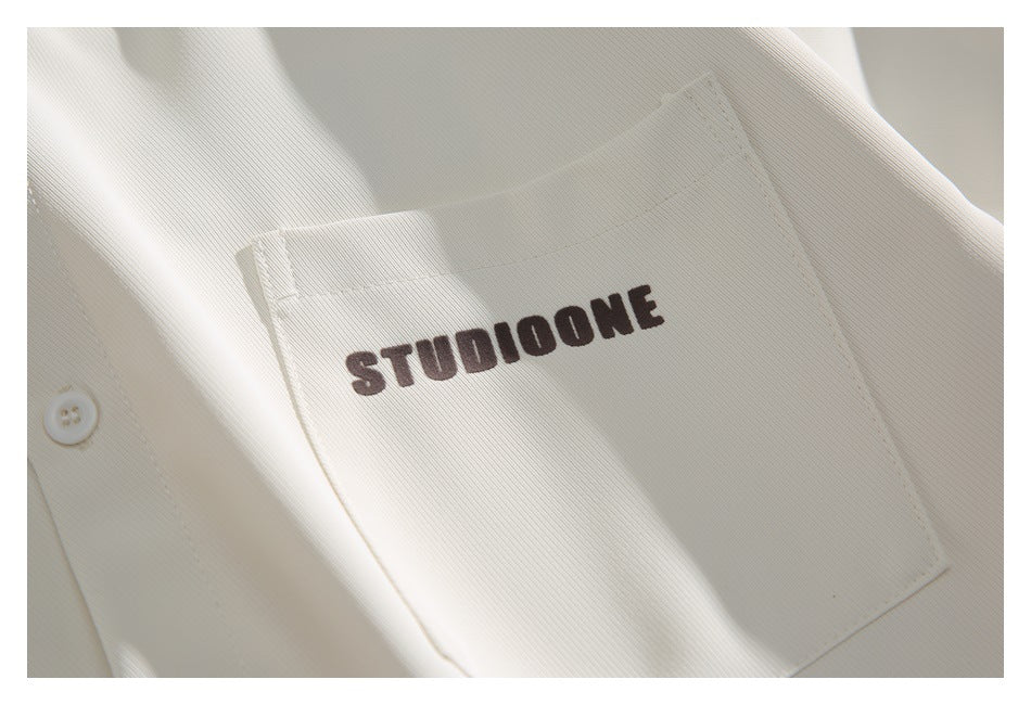 Close-up of an ivory shirt chest pocket with dark STUDIOONE lettering and a white button nearby.