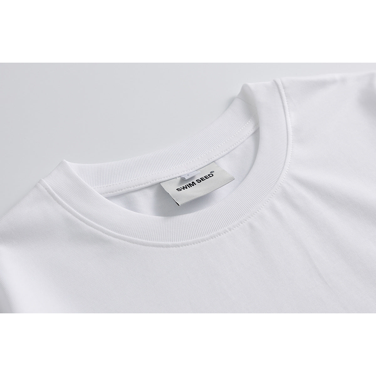 Close-up of a white T-shirt's ribbed crew neck and inner SWIM SEED label.