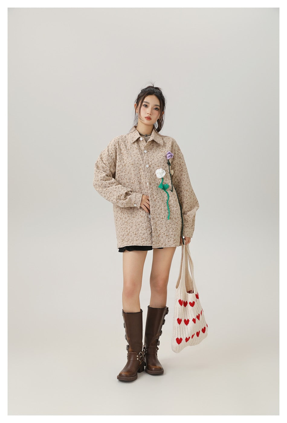 Model wearing a buttoned light khaki floral textured shirt with crochet flowers, black shorts and brown boots