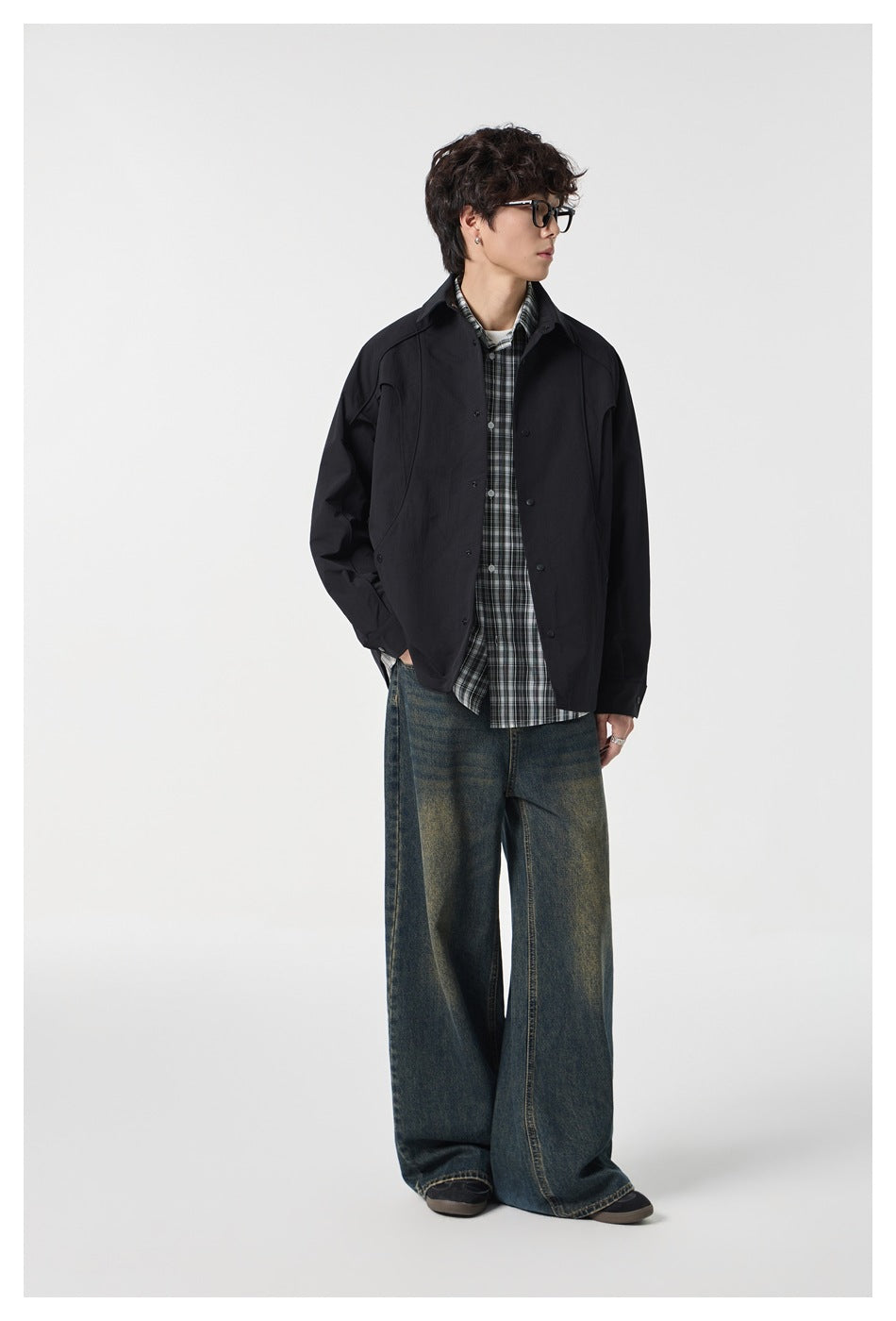 Three-quarter view of a model wearing a black collared jacket over a plaid shirt and wide-leg jeans.