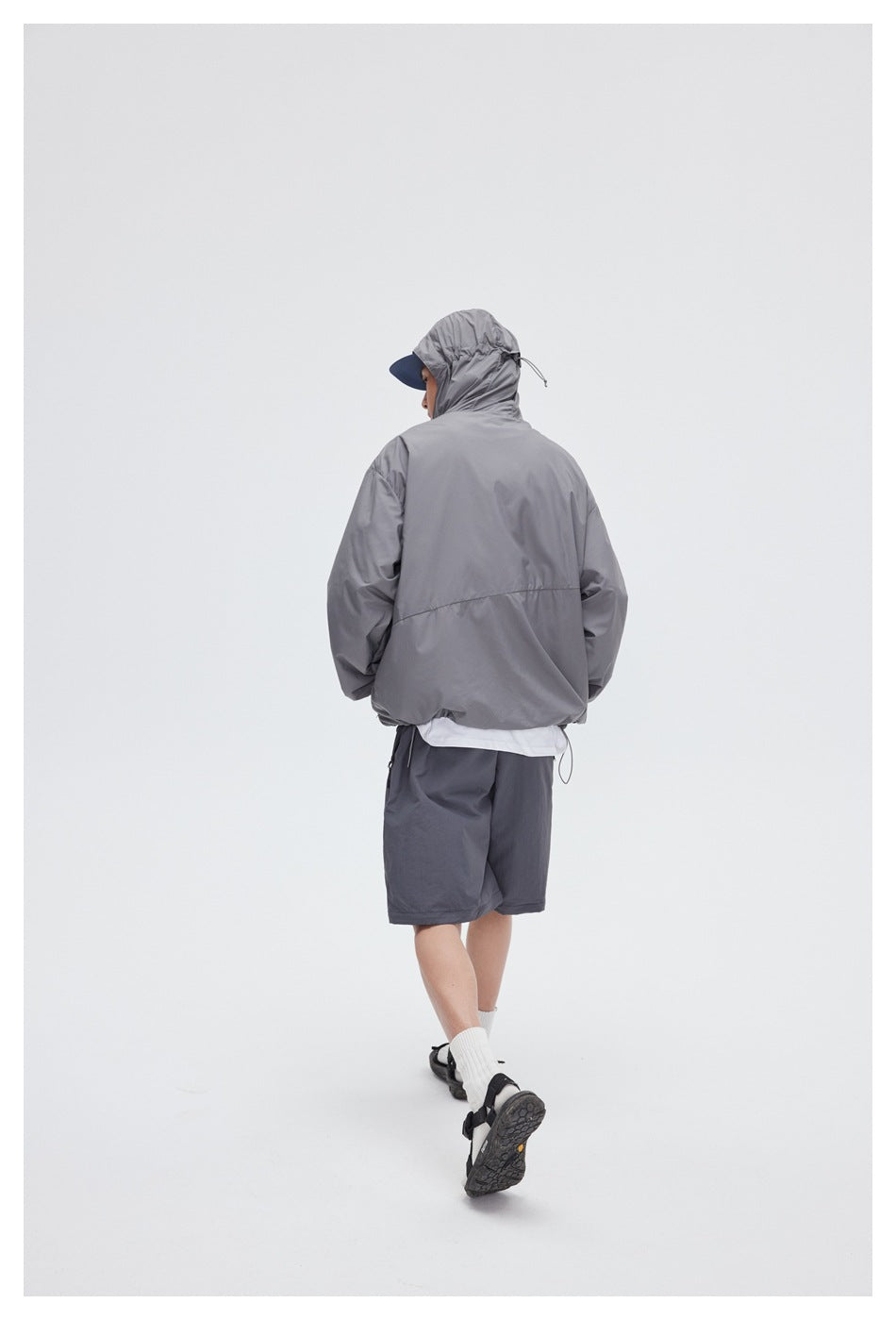 Rear view of a person wearing a gray hooded windbreaker and dark gray shorts.