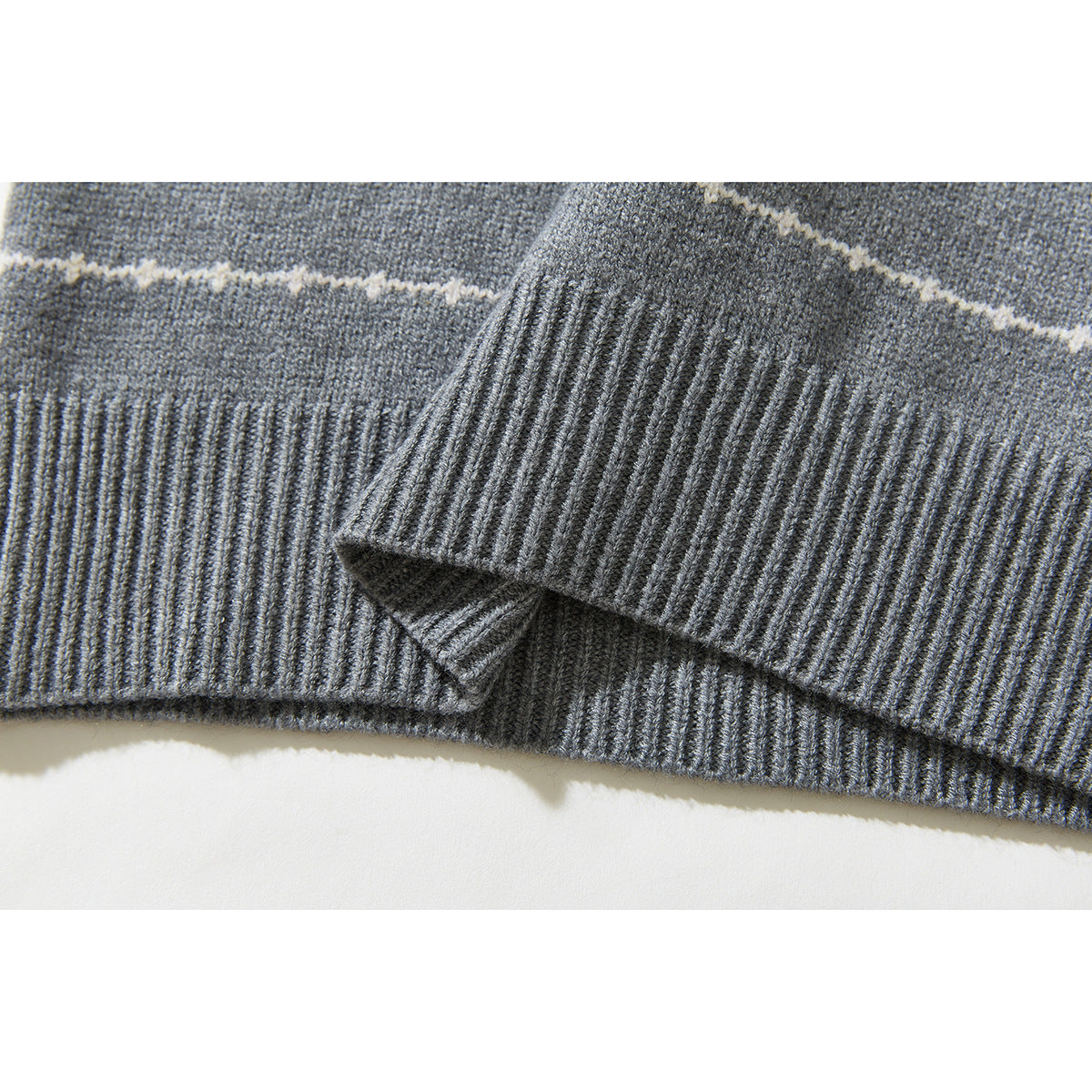 Close-up of a gray knit sweater's ribbed hem and cuff with a thin cream stripe.