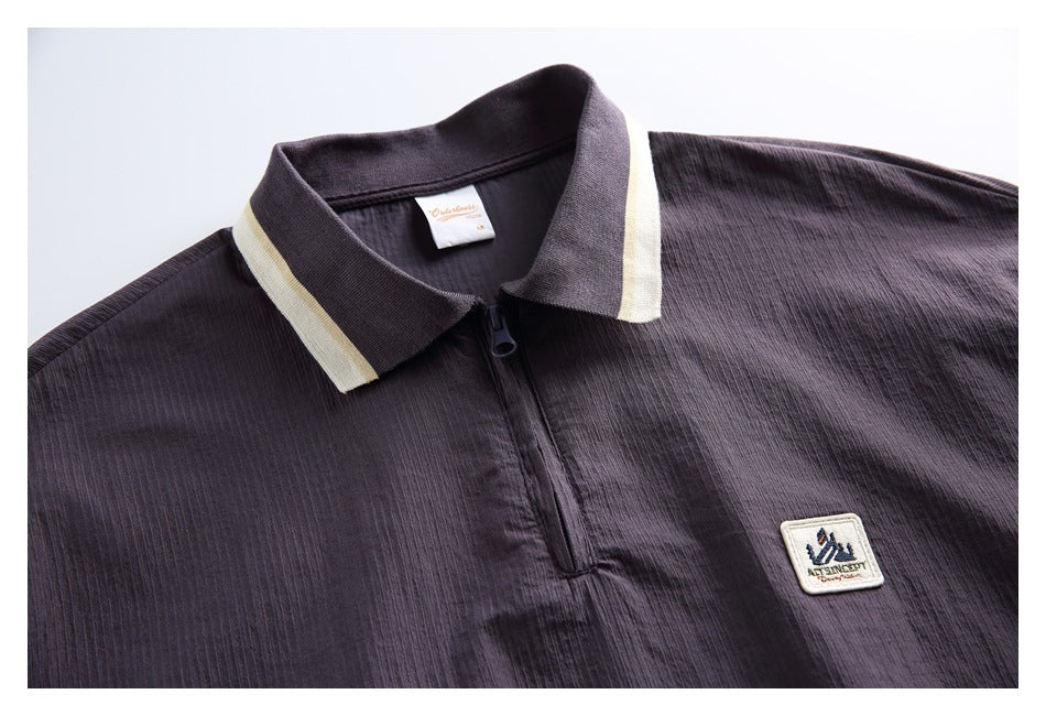 Close-up of a charcoal pullover showing its cream-trimmed collar, quarter zipper, chest patch, and neck label.